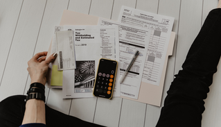 Hand holding tax documents and calculator on the ground.